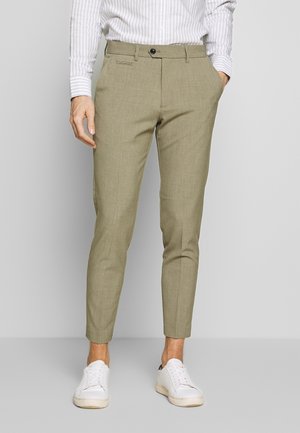 Kaki tapered broeken met een subtiele textuur, voorzien van een enkele knoopsluiting en schuine zijzakken, gecombineerd met witte sneakers.