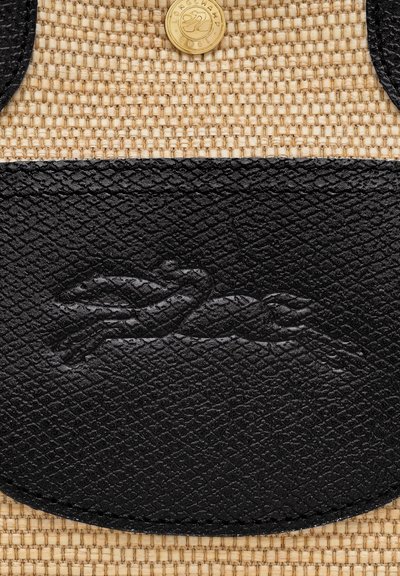 Geflochtene Strohtasche mit einem schwarzen Lederboden und einer Tasche, die ein dezentes geprägtes Logo und ein rundes goldfarbenes Hardware-Detail aufweist.