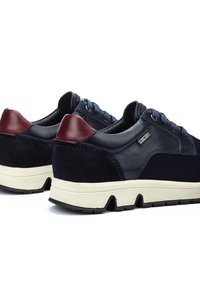 Baskets bleu marine avec des accents en cuir et en suède, une semelle crème et des lacets foncés ; dotées d'une semelle texturée et d'un capuchon de talon maroon contrastant.