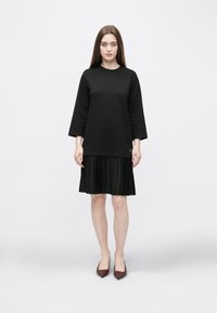 Czarna bluzka z długim rękawem połączona z plisowaną czarną spódnicą, charakteryzująca się gładką fakturą, prostym wzornictwem oraz szpiczastymi bordowymi butami.