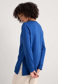 Kék, hosszú ujjú pulóver, kerek nyakkivágással, oldalhasítékokkal és bordázott mandzsettával, puha pamut keverékből készült.