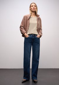 Světle růžová velurová bunda na zip, béžový top a tmavě modré džíny s širokými nohavicemi a předními kapsami; doplněné černými balerínami se špičatou špičkou.