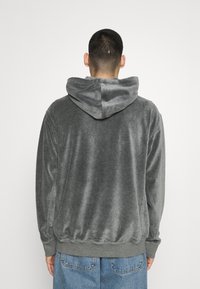Sudadera gris con una textura suave y aterciopelada, que presenta una capucha con cordón, puños acanalados y dobladillo elástico, mostrada desde la parte trasera.