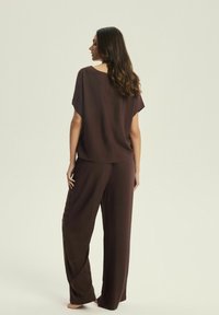 Brązowy, lekki dwuczęściowy zestaw odzieży wypoczynkowej, składający się z luźnej bluzki z krótkimi rękawami oraz spodni o szerokich nogawkach. Miękka, gładka faktura.
