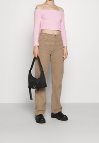 Světle růžový svetr bez ramene, zkrácený, béžové manšestrové kalhoty, černé platformové boty a malá černá taška s popruhem.