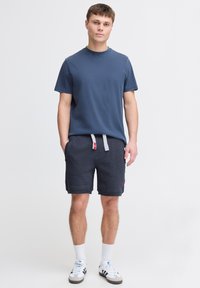 Blå kortärmad t-shirt i kombination med mörkgrå shorts som har vita dragsnören, knälånga, gjorda av mjukt tyg, bärs med vita sneakers.