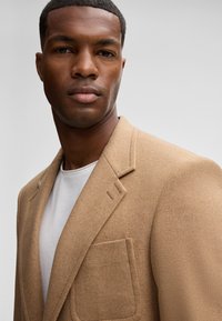 Beige Wolle Blazer mit einem Reverskragen, einer einzelnen Tasche und glatter Textur. Trägt man über einem weißen T-Shirt mit enganliegendem Design.