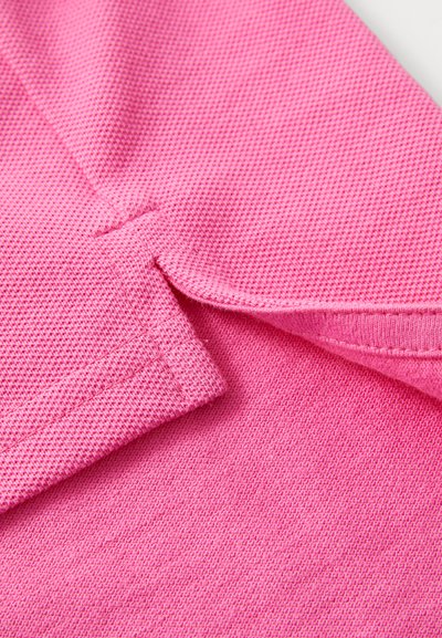 Prim-plan al unei țesături roz texturate pliată pentru a evidenția detaliile cusăturilor și tivului.