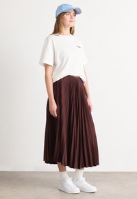 Hvit t-skjorte, burgunder plisserte skjørt, blå caps, hvite sneakers og hvite sokker. Skjørtet har en belte med "LACOSTE"-merke.
