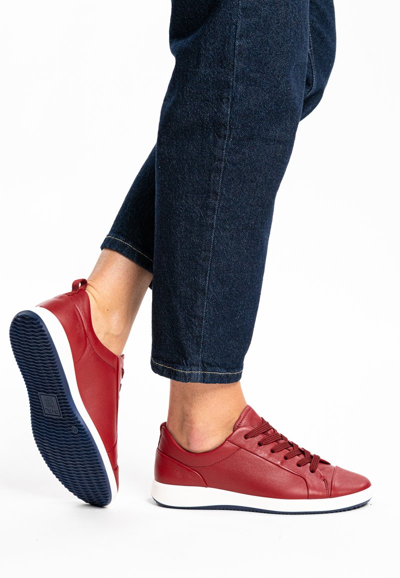 Red leather sneakers with a rounded toe and flat white rubber sole. Features lace-up closure and a textured blue outsole. Casual design.