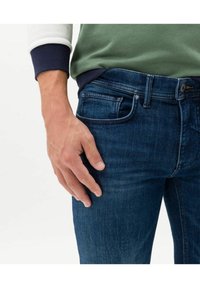 Denim jeans in dark blue with a slim fit. Features include standard pockets, a button closure, and subtle texture in the fabric.