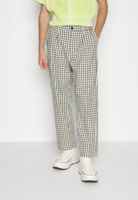 Checked trousers in black and white with pleats, featuring a button fastening, high-waisted design, and slightly tapered legs.