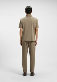 Jasnobrązowa koszulka polo z krótkimi rękawami, w połączeniu z dopasowanymi spodniami. Gładki materiał o luźnym kroju oraz podwinięte mankiety w spodniach.