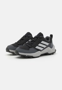 Black athletic shoes with a mesh upper, gray accents, and three white stripes. Features a rugged sole for traction and a pull tab on the heel.