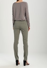 Langärmeliges, weiches graues Oberteil kombiniert mit eng geschnittenen, olivgrünen Hosen. Die Hosen haben Gesäßtaschen; das Outfit wird mit schwarzen High Heels vervollständigt.