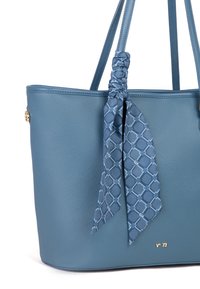 Borsa a tracolla blu con una texture, dotata di due manici lunghi, accentuata da un nastro blu a fantasia annodato di lato e un dettaglio in oro con il logo nella parte inferiore.