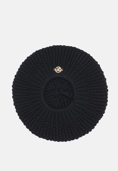 Béret noir tricoté avec motif texturé et petit emblème décoratif rond doré au centre devant.