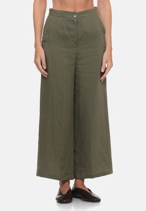 Donna che indossa pantaloni vita alta, gamba larga, verde oliva con chiusura a bottoni, abbinati a scarpe basse marrone scuro.