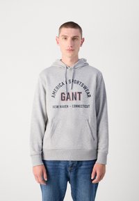 Sudadera gris con capucha y bolsillo tipo canguro, que presenta un diseño de texto gráfico multicolor. Tejido suave con puños y dobladillo acanalados.