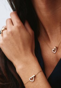 Zlata nakitna garnitura, ki vključuje obesek v obliki srca in ujemajočo se zapestnico z diamantnimi poudarki na ženskem zapestju in vratu.