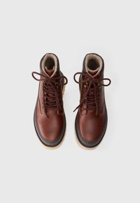 Bottines en cuir marron avec doublure en fourrure, bout rond, lacets marron et semelle en caoutchouc. Oeillets en métal et accents beige contrastants visibles.