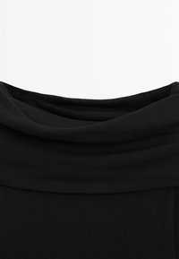 Top nero in tessuto a coste con scollatura a cascata. La texture sembra morbida ed elastica, senza motivi visibili o hardware.