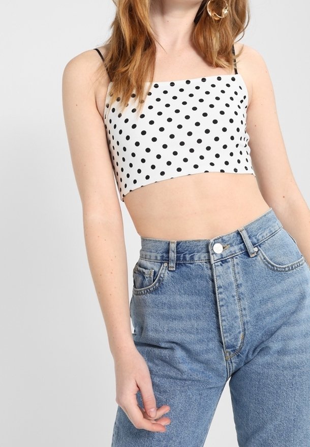 Svart prickig kort topp på en vit bakgrund, kombinerad med högmidjade blå denimjeans. Toppen har tunna band och fyrkantig utringning.
