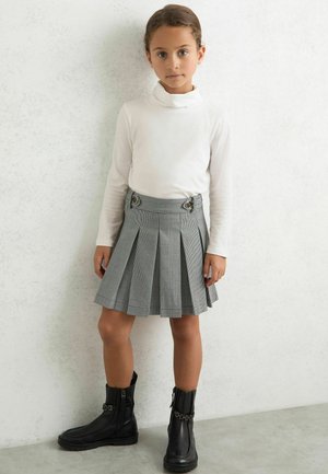 Pullover alb cu mânecă lungă și guler înalt, asociat cu o fustă plisată gri cu un model houndstooth și accente metalice. Botine negre la gleznă completează aspectul.