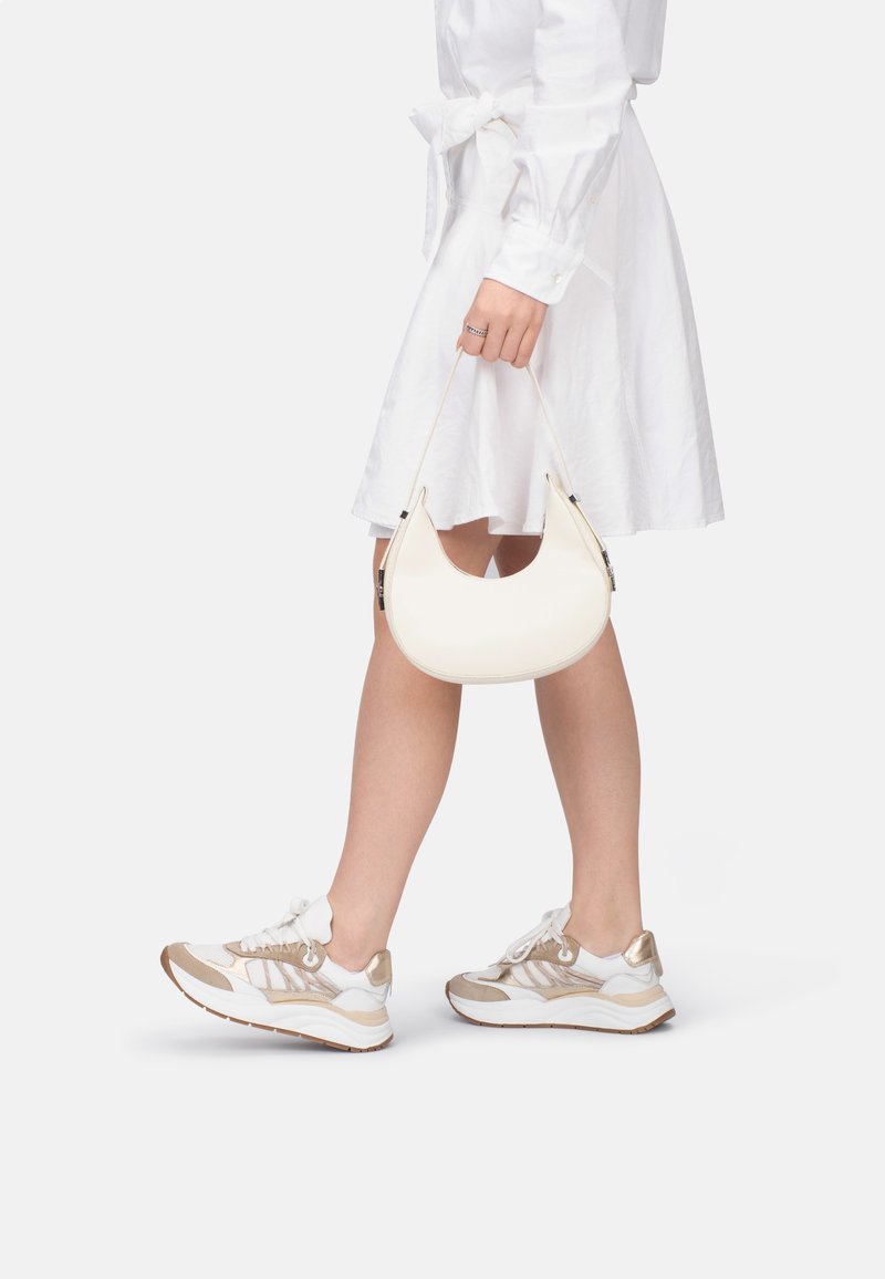 Weißer halbmondförmiger Handtasche aus glattem Material mit einem dünnen Trageriemen. Getragen zu einem weißen Hemdkleid und Sneakern mit Beigefarbenen Akzenten.