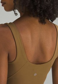 Pruun sportlik bodi madala tagaküljega, õhukeste rihmadega ja sileda tekstuuriga. Kõrval on väike logo vasakul küljel.