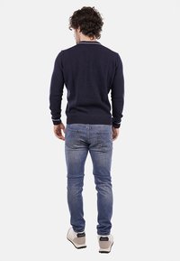 Maglione navy con polsini e orlo a coste, abbinato a jeans azzurri e sneakers grigie. Il maglione presenta un design semplice e classico.