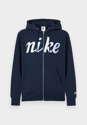 Sweat à capuche zippé marine en mélange de coton, avec un grand logo "nike" blanc, poches avant et capuche avec cordon. Texture douce.