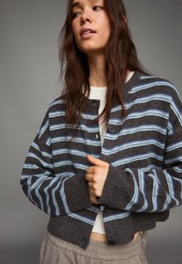 Szary kardigan w paski z jasnoniebieskimi akcentami, z zapięciem na guziki i szerokimi mankietami. Miękka tekstura i krótki fason.