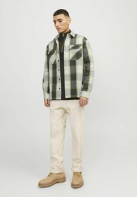 Camicia a scacchi grigia, nera e gialla con chiusura a bottoni e due tasche sul petto, abbinata a pantaloni color crema e stivali color cammello.