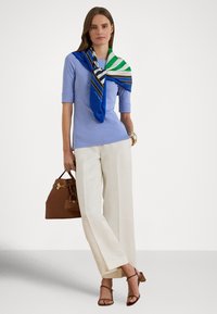 Svetlomodrý pletený top, biele široké nohavice, hnedá kabelka a modro-zeleno-biela šatka s vzorom. Celý vzhľad dopĺňajú hnedé sandále na remienkoch.