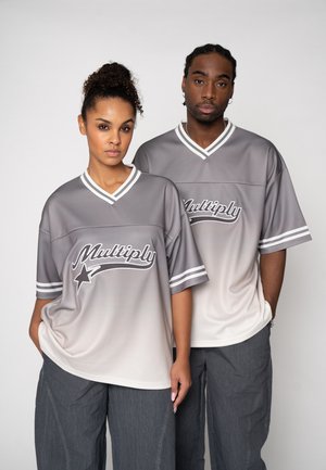 Two people, one woman and one man, wearing matching gray-to-white gradient jerseys with "Multiply" text, standing side by side against a plain background.
