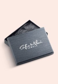Grå rektangulär smyckeslåda med en texturerad yta, delvis öppen, och avslöjar svart silkespapper inuti. Vit logotyp på locket.