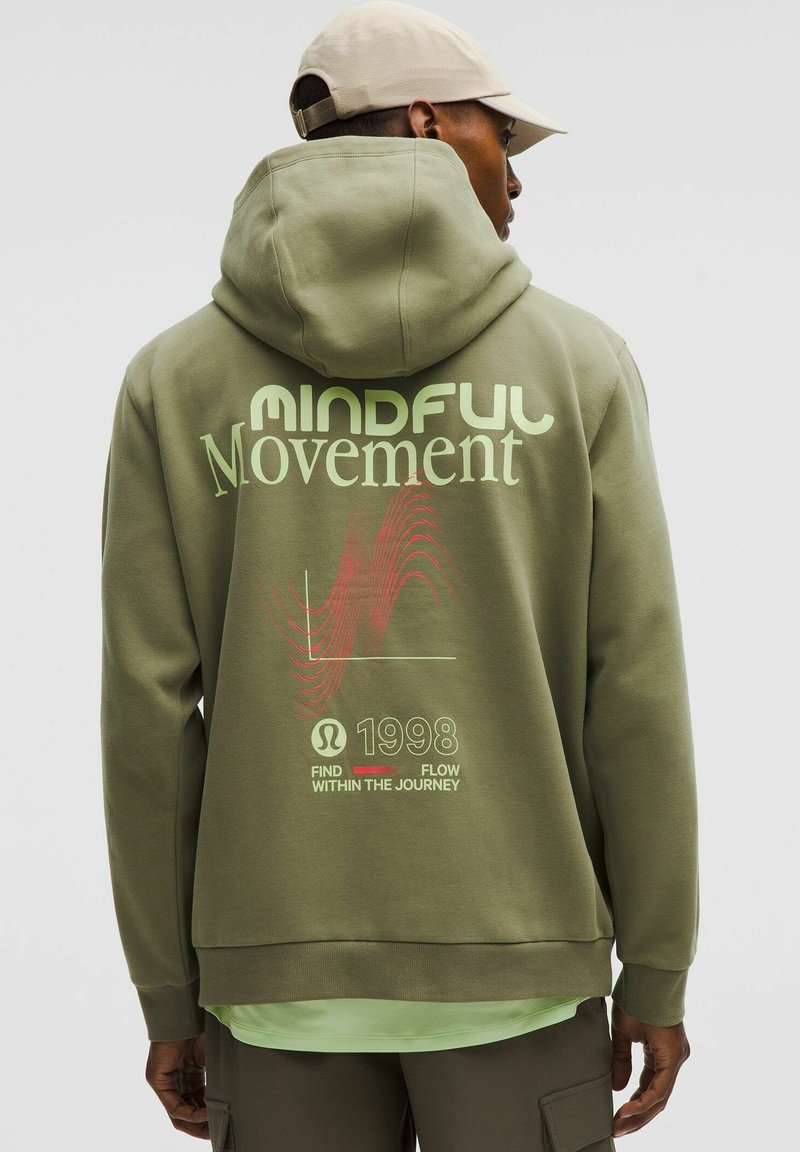 Sweat à capuche vert olive avec un grand graphique "Mouvement Conscient" en motifs vert clair et rouge au dos. Texture douce, design décontracté et coupe ample.