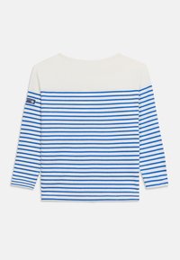 Λευκό πουκάμισο με μπλε οριζόντιες ρίγες, μανίκια 3/4 μήκους και ένα μικρό ναυτικό μπλε σημείο στο αριστερό πάνω μπράτσο.