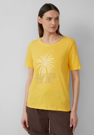 T-shirt jaune à manches courtes en tissu doux, avec un motif de palmier et le texte "LEISURE CLUB" en gris clair. Encolure ronde.
