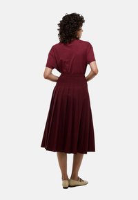 Jupe plissée bordeaux à taille haute, associée à un haut à manches courtes couleur bordeaux. Tissu lisse, longueur genou, et chaussures plates complètent le look.