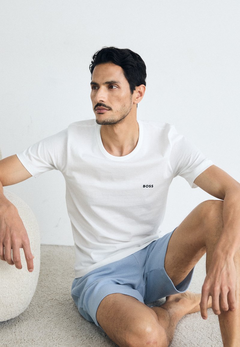 Witte katoenen t-shirt met een ronde hals en een klein zwart "BOSS" logo op de borst, gecombineerd met lichtblauwe shorts. Minimalistisch ontwerp.