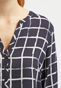 Navy blauwe blouse met een wit ruitpatroon, voorzien van een V-hals, knoopsluiting en lange mouwen gemaakt van lichtgewicht stof.
