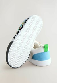 Weiße Sneaker mit blauen Wildledereinlagen und grünen Stoffakzenten, ausgestattet mit einer gemusterten Gummisohle und einem "POKEMON"-Druck an der Seite.