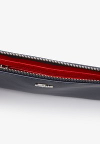 Portefeuille noir texturé avec fermeture éclair, partiellement ouvert, montrant une doublure intérieure rouge vif et des dents argentées de la fermeture éclair.