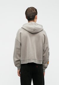 Hallhgrey lühike kapuutsiga sviiter, millel on laiad varrukad ja suur kapuuts, ning graafilised aktsendid varrukatel, kombineeritud mustade teksadega. Pehme kangastek.