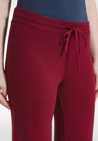 Pantalons de détente en tricot bordeaux avec une taille côtelée, dotés d'un détail à cordon de serrage et d'un tissu doux et texturé.
