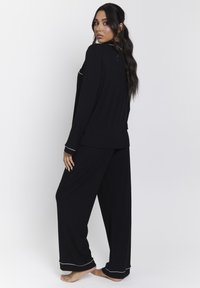Zwart loungepak bestaande uit een langwerpig shirt en een broek met wijde pijpen, voorzien van witte piping accenten. Soepele textuur en een relaxte pasvorm.