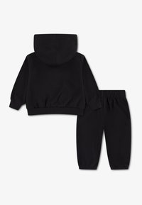 Μαύρο φούτερ με κουκούλα και αντίστοιχο παντελόνι, και τα δύο κατασκευασμένα από μαλακό ύφασμα. Το φούτερ διαθέτει ριμπ τελείωμα, ενώ το παντελόνι έχει ελαστική μέση.