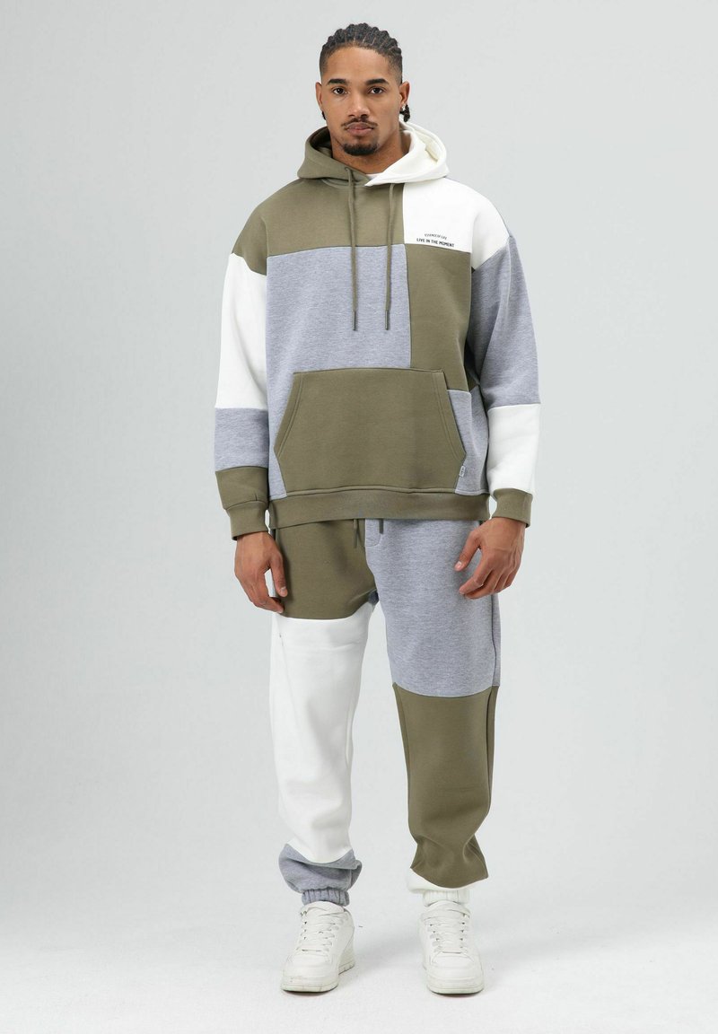 Hoodie en joggingbroek set in olijfgroen, grijs en wit. Materiaal is zacht, met een voorzak en verstelbare capuchon met trekkoorden.